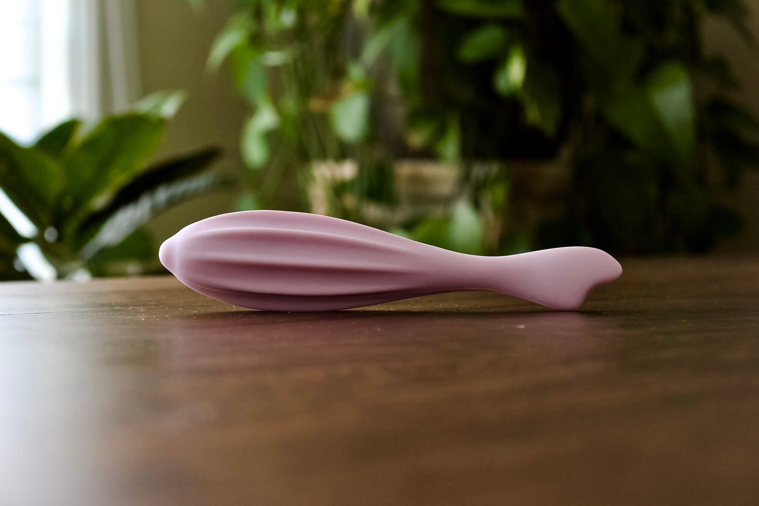 Formora Pale Lavender Face Roller resting on a brown table with sheer white curtains and lush green plants in the background – a serene skincare essential.